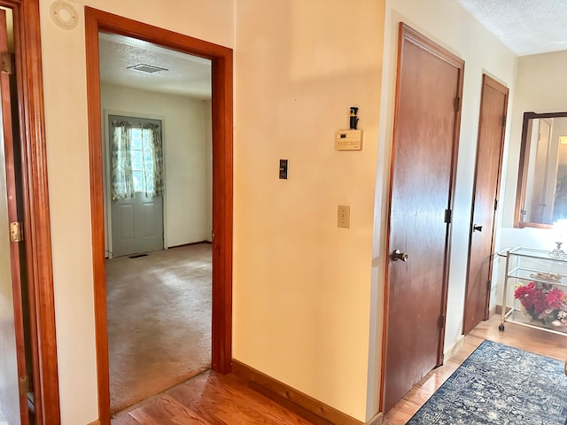 hallway with a textured ceiling and light wood-type flooring