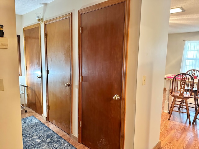 hall with light hardwood / wood-style floors and a textured ceiling