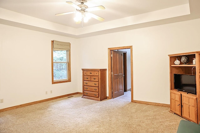 unfurnished bedroom featuring a tray ceiling, light colored carpet, and ceiling fan