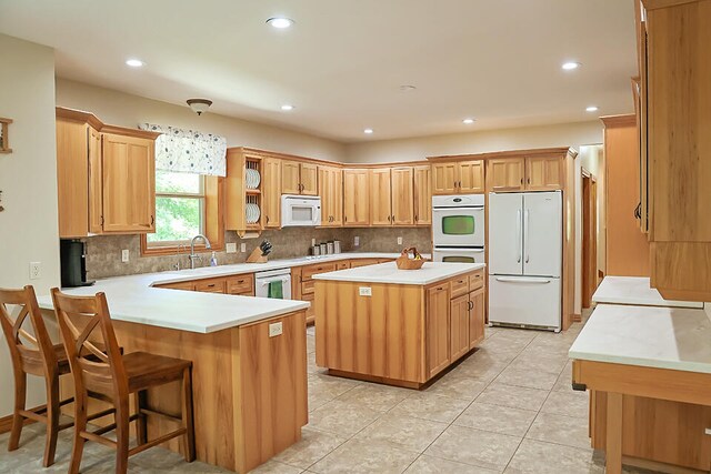 kitchen featuring a center island, white appliances, sink, a kitchen bar, and light tile patterned floors