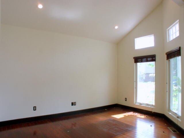 spare room with dark wood-type flooring and high vaulted ceiling