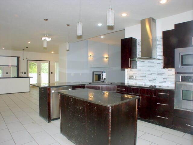 kitchen with hanging light fixtures, tasteful backsplash, a kitchen island, wall chimney range hood, and appliances with stainless steel finishes