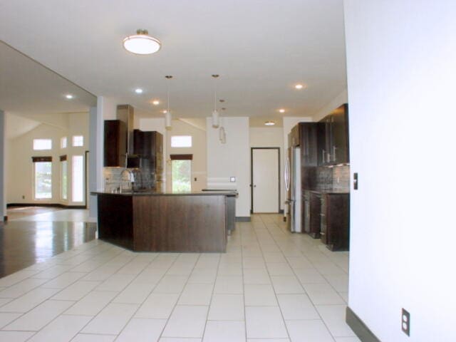 kitchen featuring hanging light fixtures, stainless steel fridge, light tile patterned floors, dark brown cabinets, and backsplash