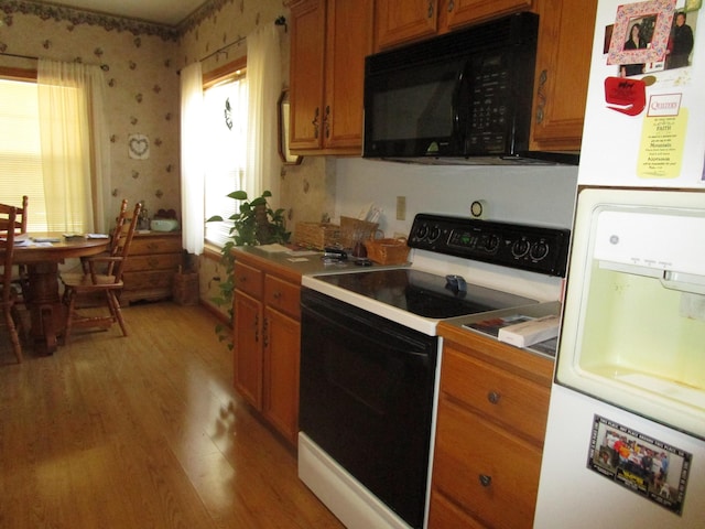 kitchen with freestanding refrigerator, light wood-style floors, brown cabinetry, black microwave, and range with electric stovetop