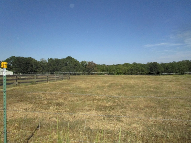 view of yard with fence, a view of trees, and a rural view