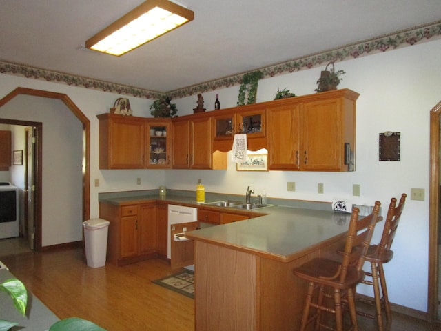 kitchen with a sink, glass insert cabinets, light wood-style flooring, a peninsula, and brown cabinetry
