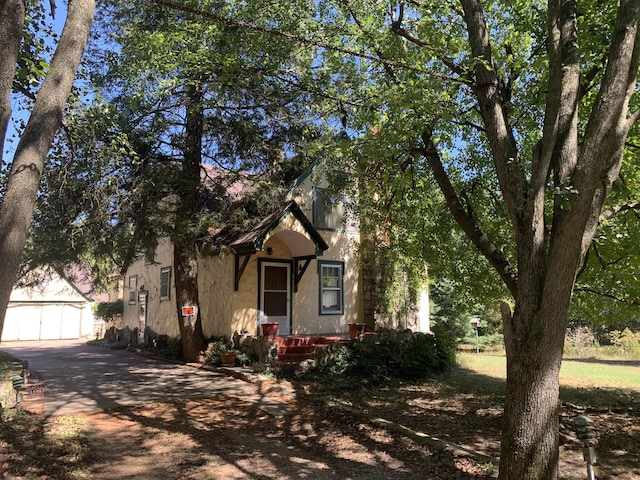 view of property hidden behind natural elements with stucco siding, an outbuilding, and aphalt driveway