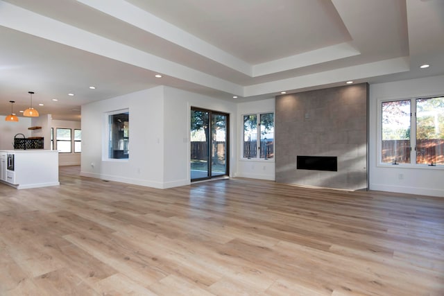 unfurnished living room with light hardwood / wood-style floors, a tile fireplace, and a raised ceiling