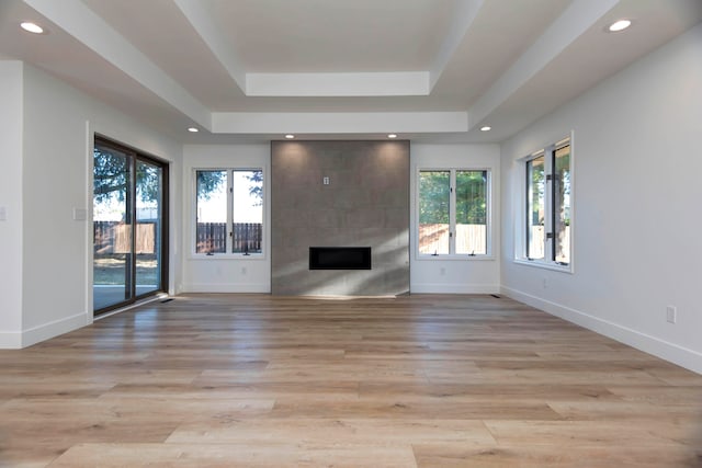 unfurnished living room featuring light hardwood / wood-style floors, a tray ceiling, and a tile fireplace