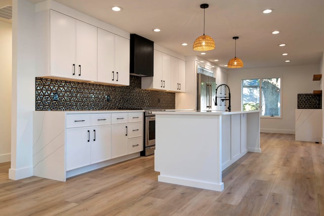 kitchen featuring appliances with stainless steel finishes, white cabinetry, a kitchen island with sink, light wood-type flooring, and decorative light fixtures