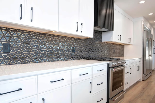 kitchen featuring wall chimney range hood, white cabinets, decorative backsplash, light hardwood / wood-style flooring, and high quality appliances