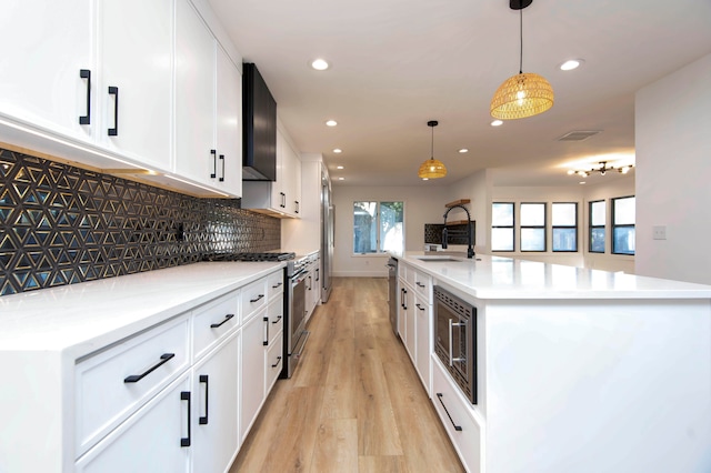 kitchen with white cabinetry, stainless steel appliances, pendant lighting, light hardwood / wood-style flooring, and a kitchen island with sink