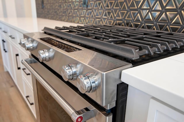 details with high end stainless steel range oven, white cabinetry, and light wood-type flooring