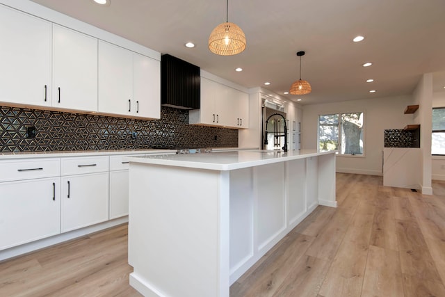 kitchen with a center island with sink, decorative light fixtures, white cabinets, light hardwood / wood-style floors, and tasteful backsplash