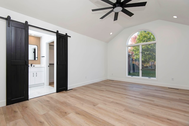 interior space featuring light hardwood / wood-style flooring, a barn door, vaulted ceiling, and a wealth of natural light