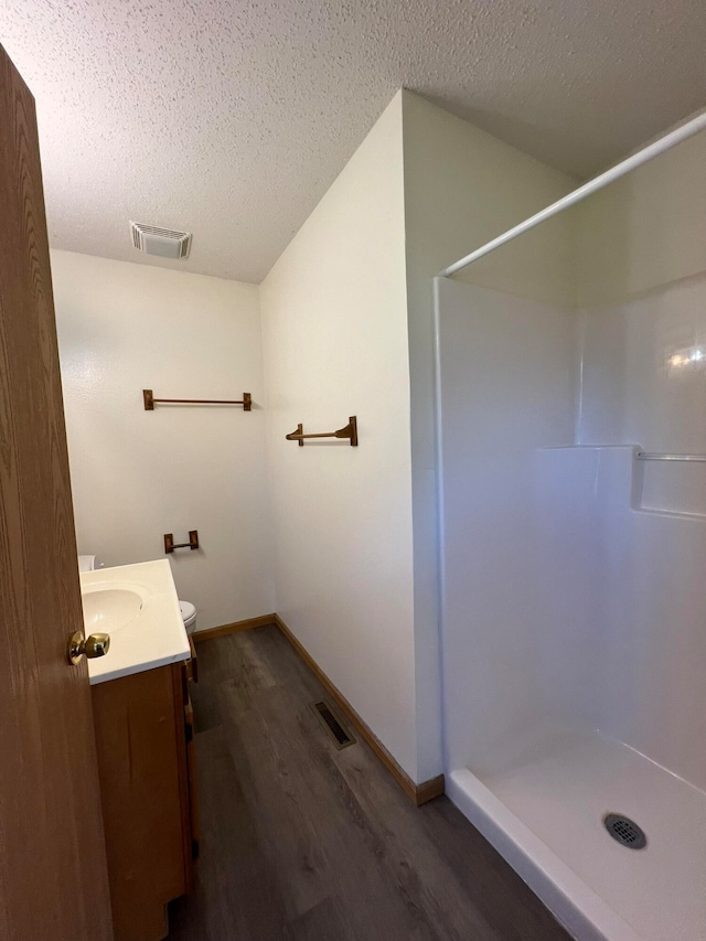 bathroom with hardwood / wood-style floors, walk in shower, vanity, and a textured ceiling