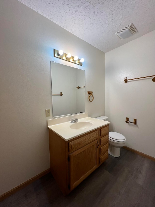 bathroom with a textured ceiling, hardwood / wood-style flooring, vanity, and toilet