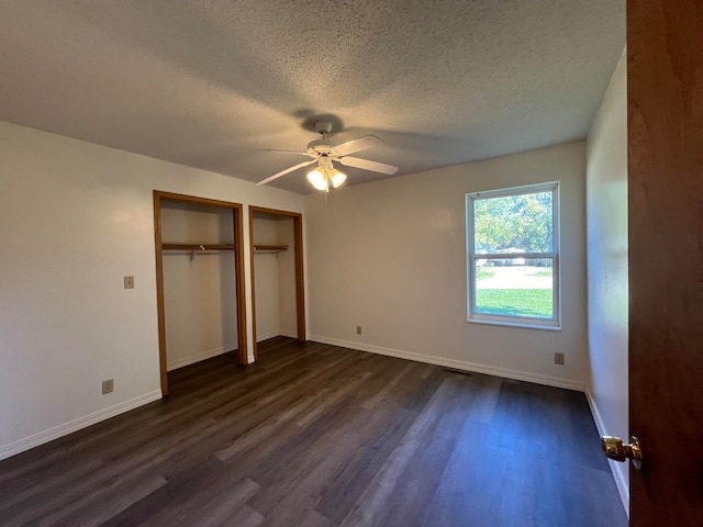 unfurnished bedroom with ceiling fan, multiple closets, a textured ceiling, and dark hardwood / wood-style floors