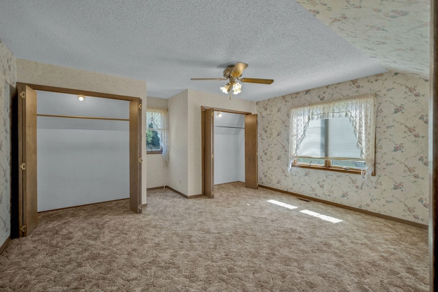 unfurnished bedroom featuring ceiling fan, multiple closets, light carpet, and multiple windows