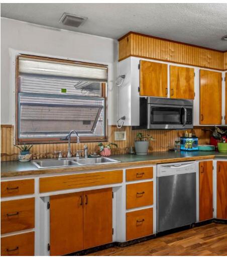 kitchen with a textured ceiling, a sink, stainless steel appliances, dark wood-style flooring, and visible vents