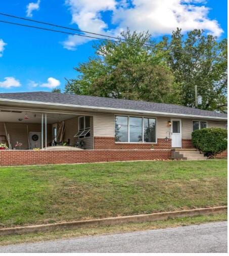 view of front of house featuring brick siding, roof with shingles, and a front yard