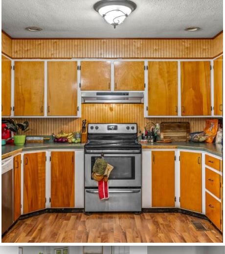 kitchen featuring stainless steel appliances, under cabinet range hood, a textured ceiling, and brown cabinetry