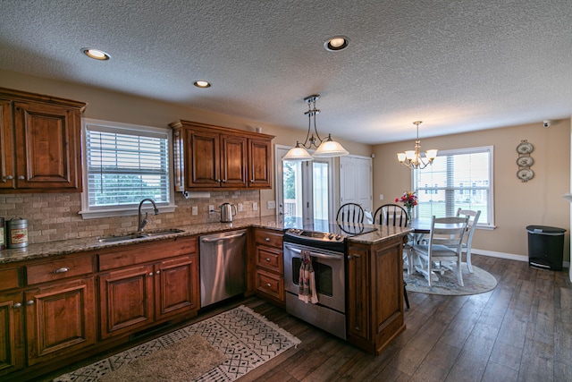 kitchen with dark wood-type flooring, sink, kitchen peninsula, appliances with stainless steel finishes, and decorative light fixtures