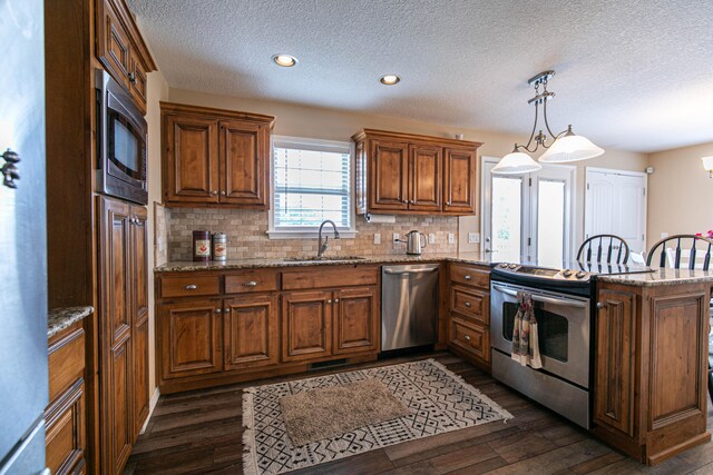 kitchen featuring dark wood-type flooring, sink, kitchen peninsula, hanging light fixtures, and appliances with stainless steel finishes