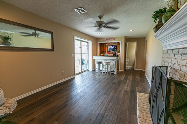 unfurnished living room featuring a fireplace, ceiling fan, dark wood-type flooring, and a textured ceiling