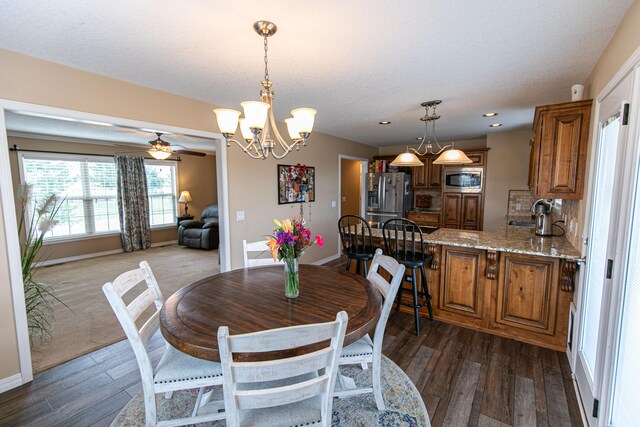 dining area with ceiling fan with notable chandelier, a textured ceiling, and dark hardwood / wood-style flooring