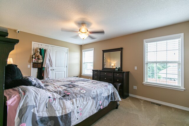 bedroom featuring a closet, light colored carpet, multiple windows, and ceiling fan