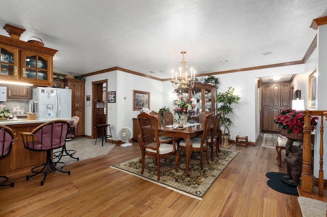 dining room featuring an inviting chandelier, light wood-type flooring, crown molding, and a textured ceiling