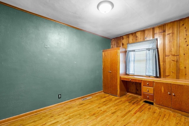 unfurnished bedroom featuring wood walls, light hardwood / wood-style flooring, and built in desk