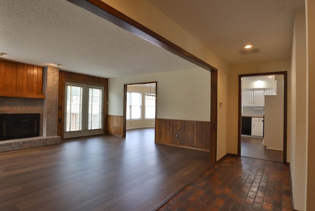 unfurnished living room with a brick fireplace, dark wood-type flooring, wood walls, and a textured ceiling