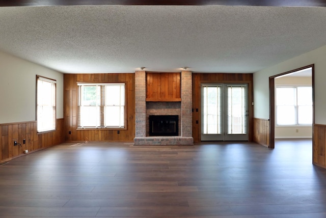 unfurnished living room with a brick fireplace, a textured ceiling, wood walls, and dark hardwood / wood-style flooring