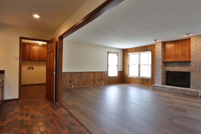 unfurnished living room with a fireplace, dark hardwood / wood-style floors, wooden walls, and a textured ceiling