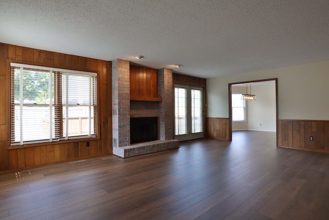 unfurnished living room featuring a brick fireplace, wooden walls, dark hardwood / wood-style floors, and a textured ceiling