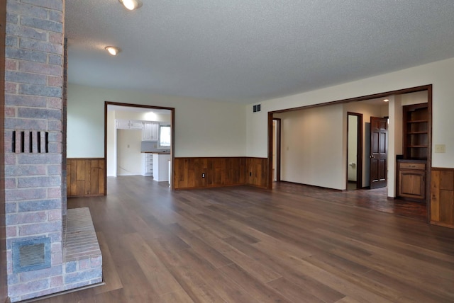 unfurnished living room with wood walls, dark hardwood / wood-style floors, and a textured ceiling