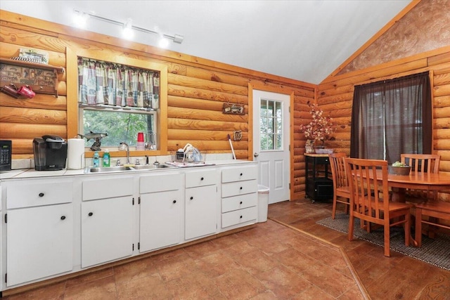 kitchen featuring lofted ceiling, rustic walls, and white cabinetry