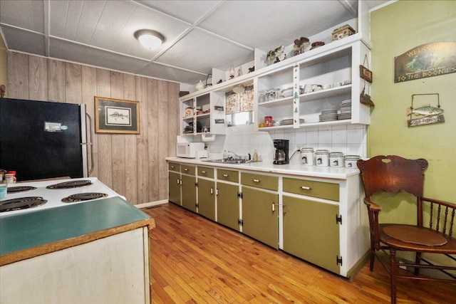 kitchen featuring black fridge, sink, wooden walls, light hardwood / wood-style flooring, and decorative backsplash