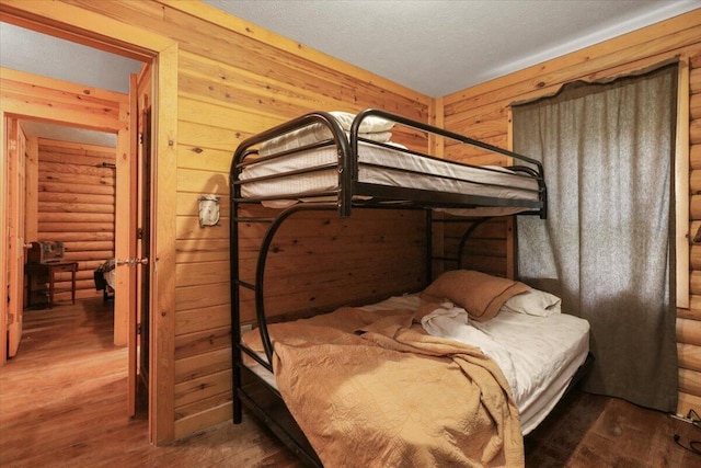 bedroom with wooden walls, hardwood / wood-style floors, and a textured ceiling