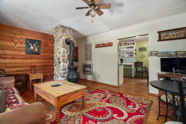 living room featuring ceiling fan, log walls, a wood stove, hardwood / wood-style flooring, and heating unit