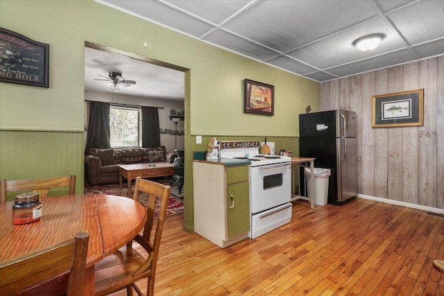 kitchen with stainless steel refrigerator, light wood-type flooring, ceiling fan, wooden walls, and electric stove