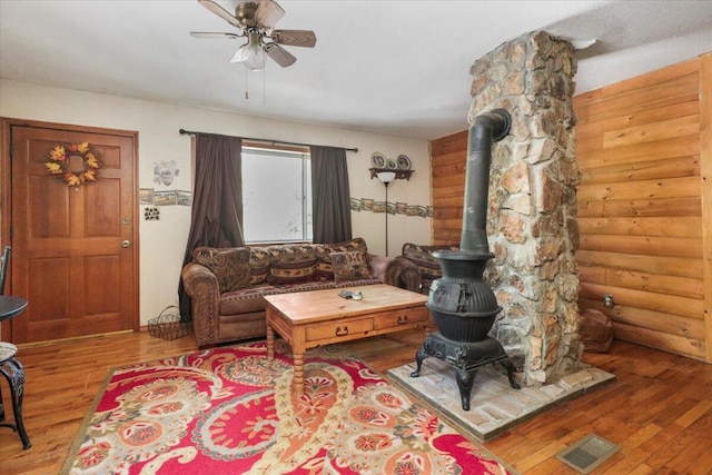 living room with ceiling fan, hardwood / wood-style flooring, rustic walls, and a wood stove