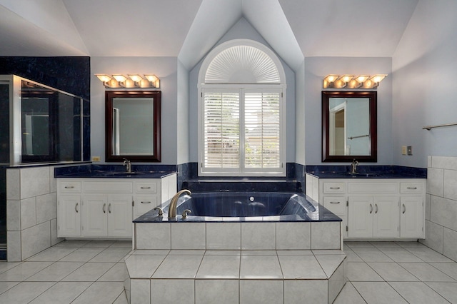 bathroom with tile patterned floors, vaulted ceiling, vanity, and tiled bath