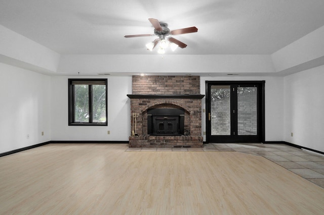 unfurnished living room featuring a wood stove, ceiling fan, and light hardwood / wood-style floors