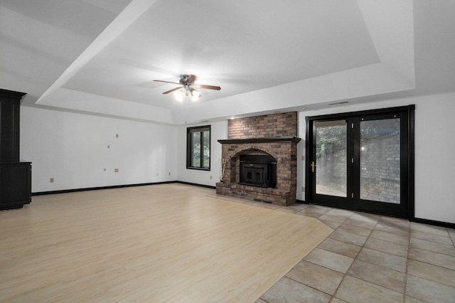 unfurnished living room with ceiling fan, a raised ceiling, light wood-type flooring, and a wood stove