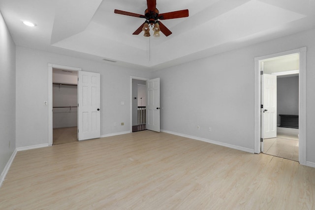 unfurnished bedroom featuring ceiling fan, a raised ceiling, a closet, a spacious closet, and light hardwood / wood-style floors