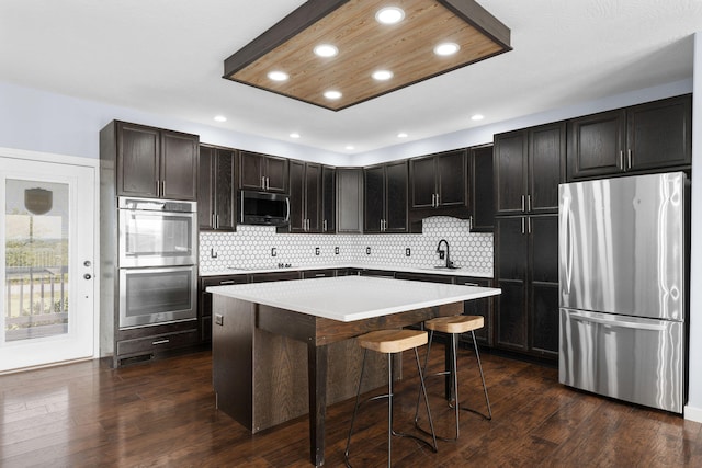 kitchen with sink, a breakfast bar, stainless steel appliances, dark hardwood / wood-style floors, and a center island