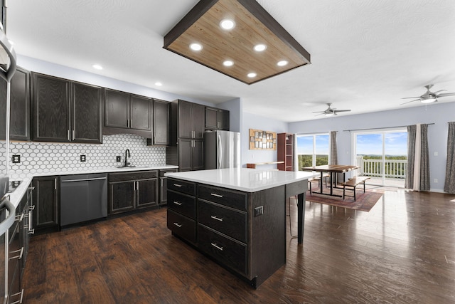 kitchen featuring a kitchen island, dark hardwood / wood-style flooring, backsplash, appliances with stainless steel finishes, and a kitchen bar